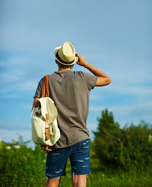 La parte trasera del joven y atractivo hombre con estilo moderno en ropa casual con sombrero en gafas detrás del cielo azul