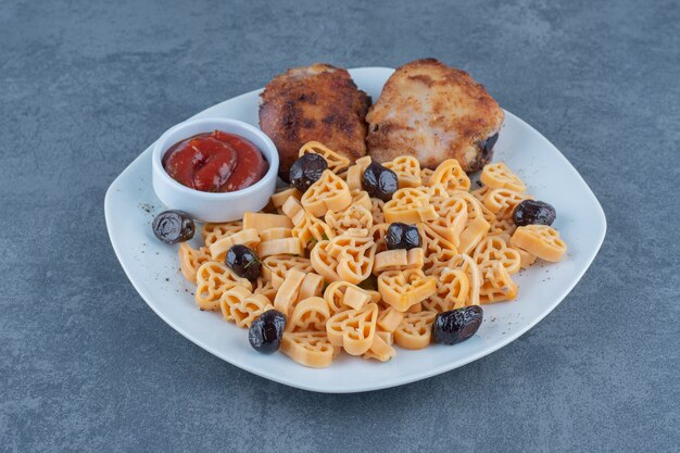 Partes de pollo a la parrilla y macarrones en un plato blanco.