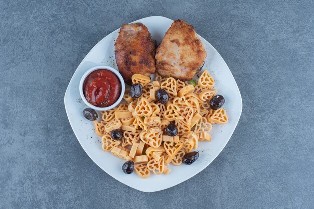 Partes de pollo a la parrilla y macarrones en un plato blanco.