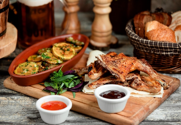 Partes de pollo a la parrilla servidas con rodajas de papa asadas y salsas