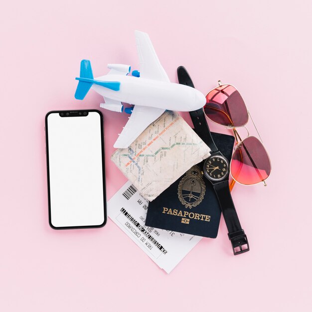 Pasaporte; mapa; Entradas; avión de juguete; reloj de pulsera; Teléfono móvil y gafas de sol sobre fondo rosa