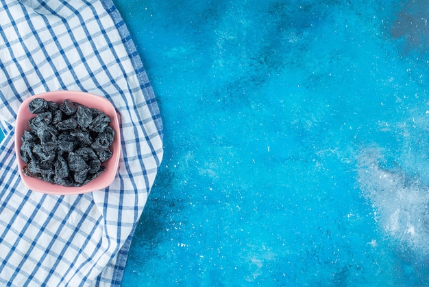 Pasas negras en un recipiente sobre un paño de cocina, sobre la mesa azul.