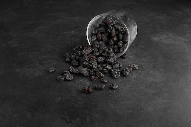 Foto gratuita pasas sultanas secas negras de un vaso sobre fondo negro.