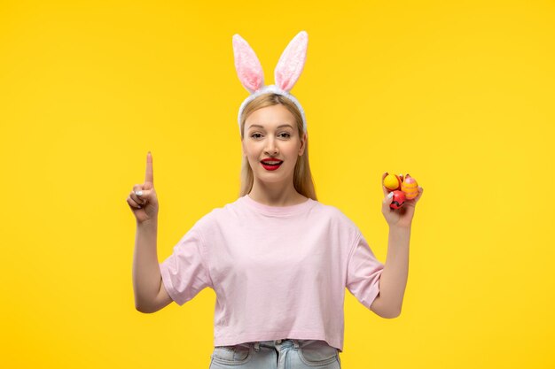 Pascua hermosa linda chica rubia con orejas de conejo sonriendo y sosteniendo huevos de pascua