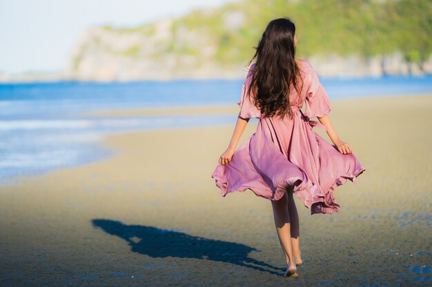 Paseo feliz de la sonrisa asiática joven hermosa de la mujer del retrato en el mar al aire libre tropical de la playa de la naturaleza