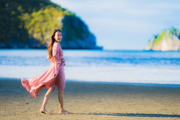 Paseo feliz de la sonrisa asiática joven hermosa de la mujer del retrato en el mar al aire libre tropical de la playa de la naturaleza