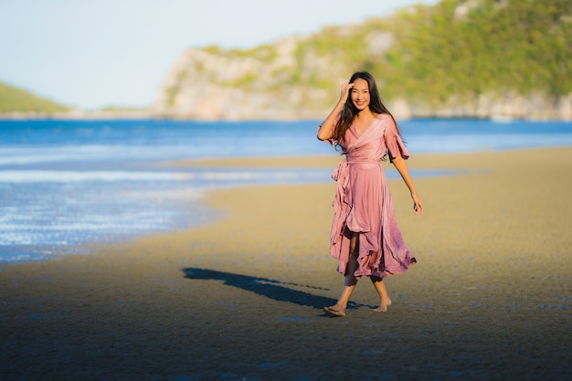 Paseo feliz de la sonrisa asiática joven hermosa de la mujer del retrato en el mar al aire libre tropical de la playa de la naturaleza