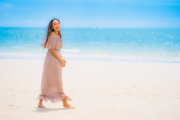 Paseo feliz de la sonrisa asiática joven hermosa de la mujer del retrato en el mar al aire libre tropical de la playa de la naturaleza