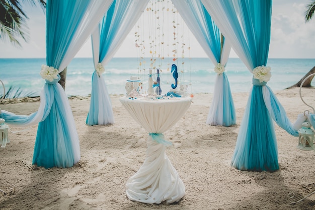 Pasillo de boda azul y blanco en una playa rodeada de palmeras con el mar al fondo