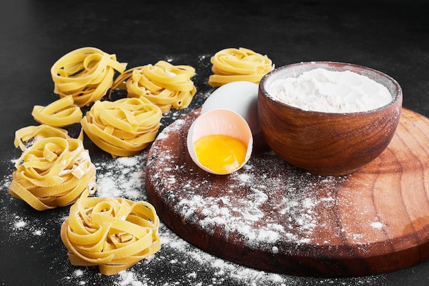 Foto gratuita pasta aislada en negro con una taza de harina y huevo a un lado.