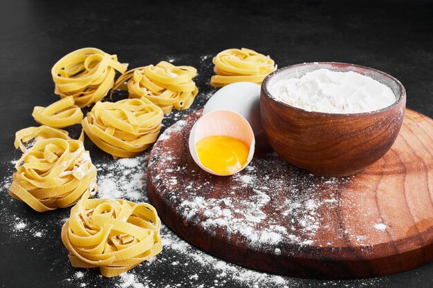 Pasta aislada en negro con una taza de harina y huevo a un lado.