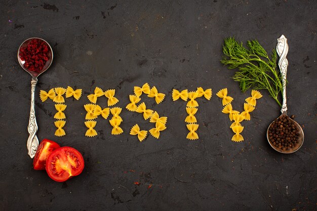 Pasta amarilla cruda sabrosa palabra en forma junto con rodajas de tomates y verduras en un piso gris