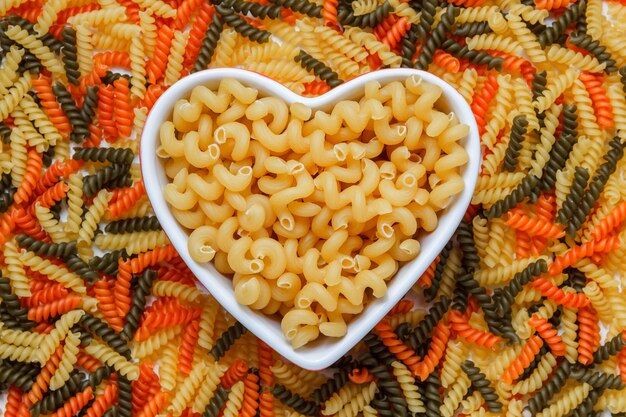 Pasta cellentani en un plato en forma de corazón sobre una mesa fusilli de color. vista superior.