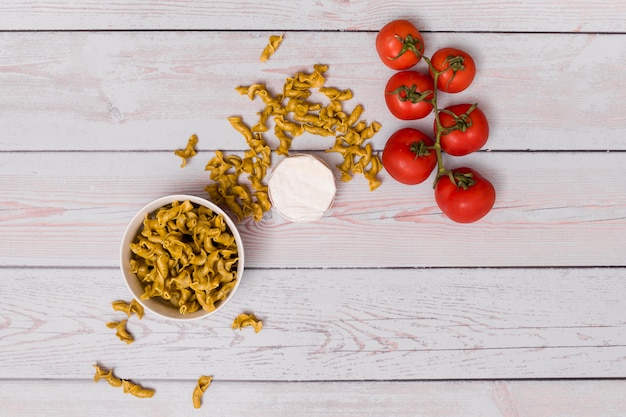 Pasta sin cocer; Tomates rojos y contenedor cerrado sobre mesa de madera