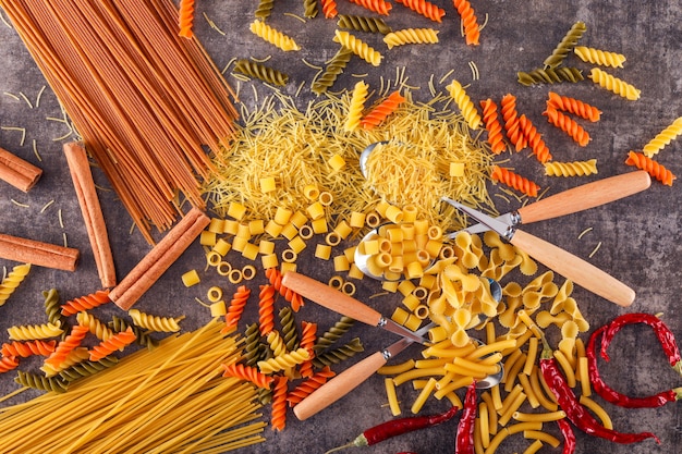 pasta de color mixto con cuchara tenedor pimienta sobre superficie gris