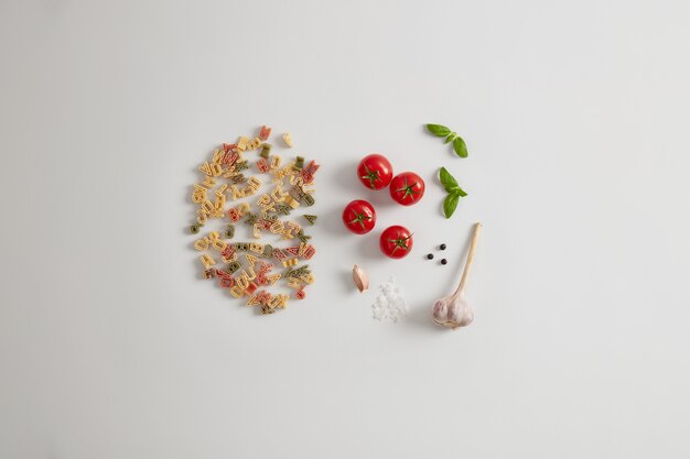 Pasta colorida de grano entero con forma de letra aislada sobre fondo blanco con tomates, sal marina, ajo, granos de pimienta, alto contenido de cangrejos. Coberturas saludables para su pasta como verduras, grasas, proteínas.