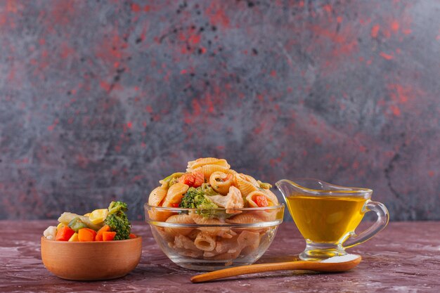 Pasta de concha italiana con aceite y ensalada de verduras mixtas en mesa de luz.