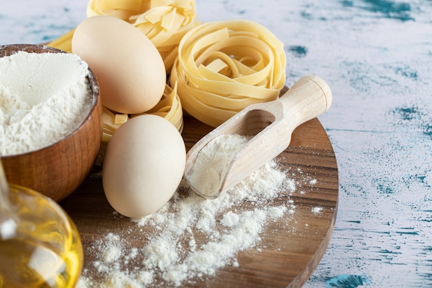 Foto gratuita pasta cruda con aceite, huevo y tazón de harina sobre tabla de madera.