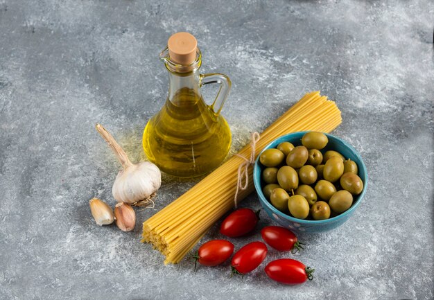 Pasta cruda, aceite y verduras frescas sobre piedra.