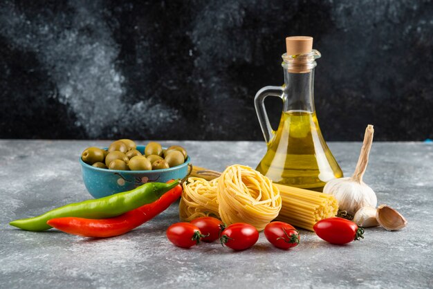 Pasta cruda, aceite y verduras frescas sobre piedra.