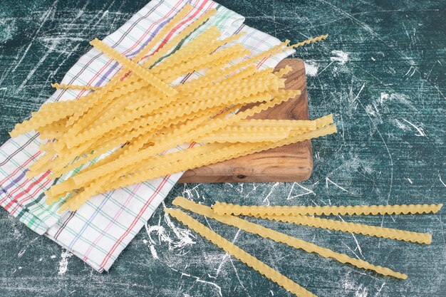 Pasta cruda amarilla con mantel sobre tabla de madera. Foto de alta calidad