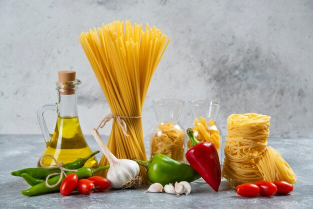 Pasta cruda con una botella de vidrio de aceite y verduras.