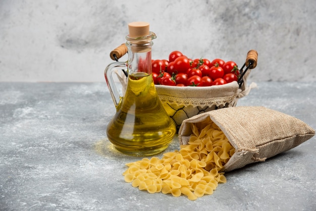 Pasta cruda con una canasta de tomates cherry y una botella de aceite de oliva.