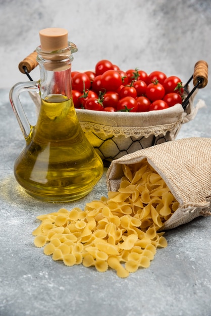 Pasta cruda con una canasta de tomates cherry y una botella de aceite de oliva.