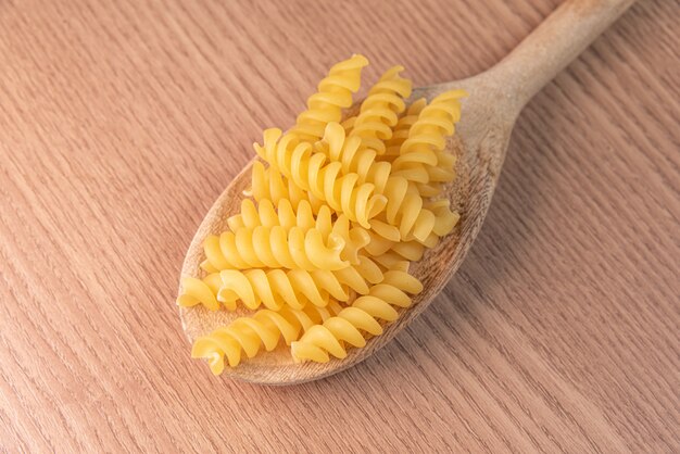 Pasta cruda en cuchara de madera en mesa de madera