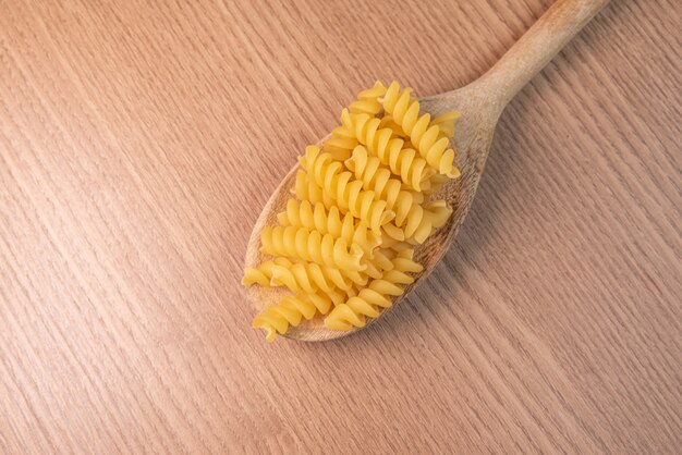 Pasta cruda en cuchara de madera en mesa de madera