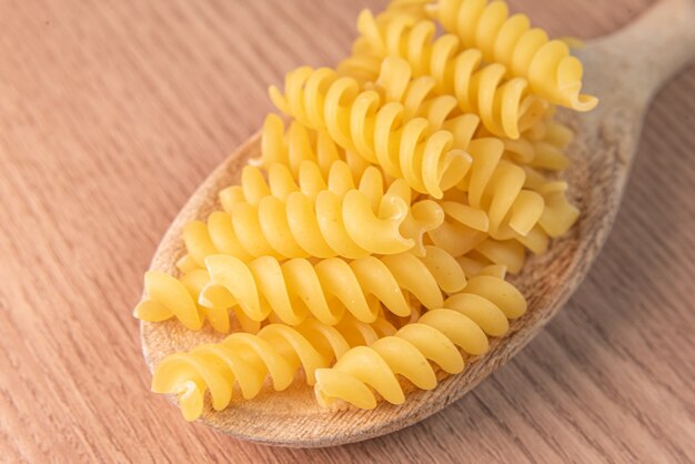 Pasta cruda en cuchara de madera en mesa de madera