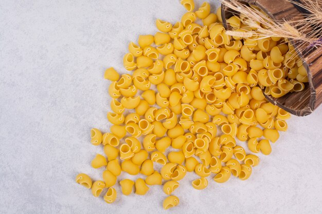 Pasta cruda en forma de concha sobre la superficie blanca con cuchara de madera