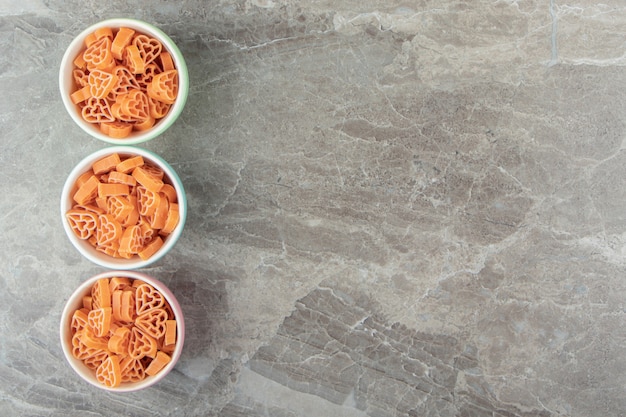 Pasta cruda en forma de corazón en tazones de colores.