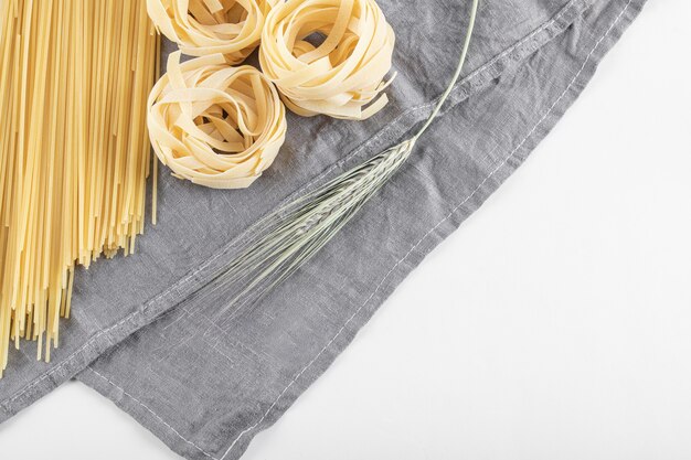 Pasta cruda de tallarines y espaguetis sobre mantel gris.