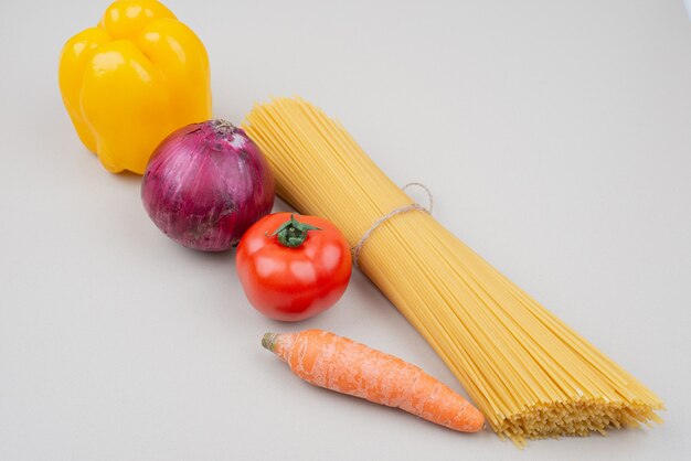 Pasta cruda con verduras sobre superficie blanca