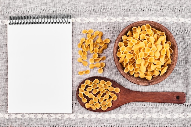 Foto gratuita pasta en una cuchara de madera con un libro de recetas a un lado.