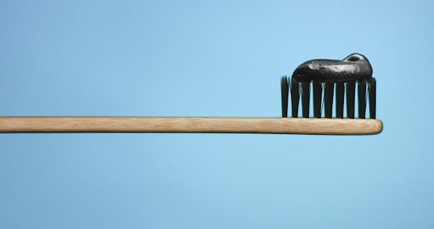 Pasta de dientes negra en el cepillo de dientes con cerdas negras y mango de madera aislado en fondos coloridos