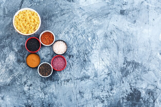 Pasta Ditalini en un recipiente con una variedad de especias vista superior sobre un fondo de yeso gris