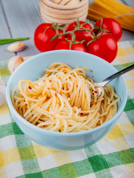 Pasta de espagueti con hojuelas de chile en un tazón blanco con tenedor y tomates frescos sobre un mantel