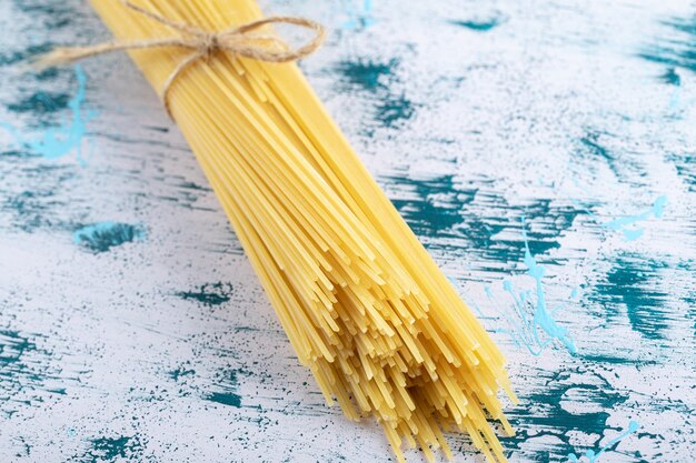 Pasta de espaguetis cruda atada con una cuerda en la superficie colorida.