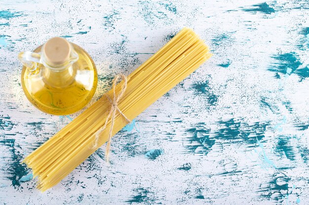 Pasta de espaguetis cruda con botella de aceite en blanco.