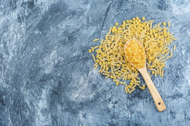 Pasta esparcida laicos plana en cuchara de madera sobre fondo de yeso sucio. horizontal