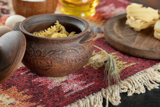 Pasta espiral sin preparar en una olla con huevos y un pequeño tazón de madera de harina