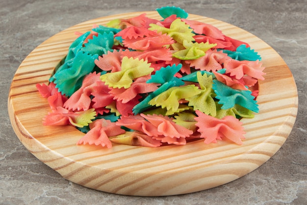 Pasta farfalle colorida en placa de madera