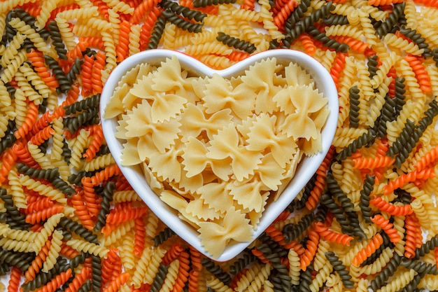 Pasta farfalle cruda en una vista superior de placa en forma de corazón sobre una mesa fusilli de color