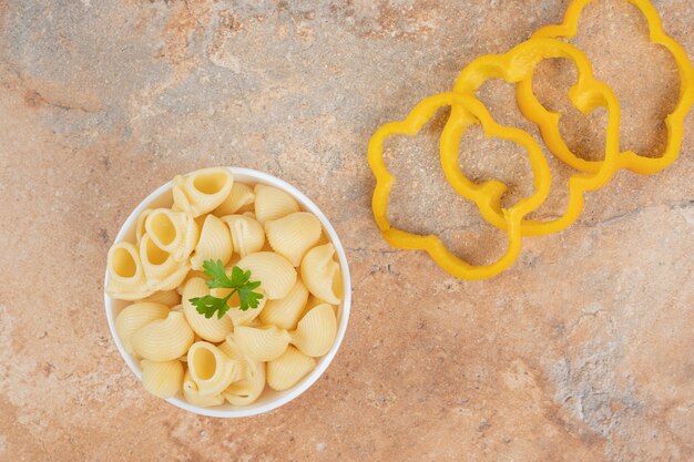 Pasta con forma de concha y rodajas de pimiento sobre fondo naranja