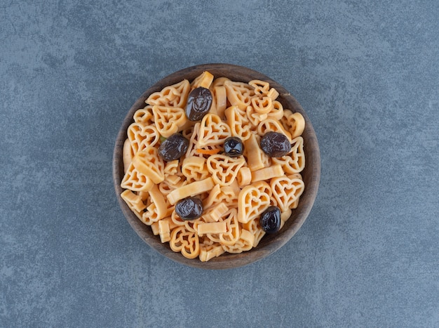 Pasta en forma de corazón con aceitunas en tazón de madera.