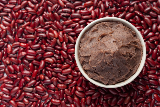 Pasta de frijoles rojos dulces en un tazón blanco colocar en el piso entre semillas de frijoles rojos