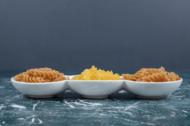 Pasta fusilli cruda amarilla y marrón en tazones blancos. Foto de alta calidad