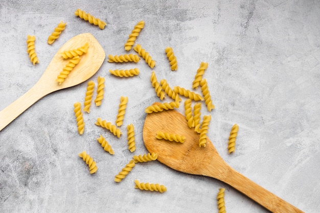 Foto gratuita pasta fusilli cruda y espátula de madera sobre fondo de hormigón